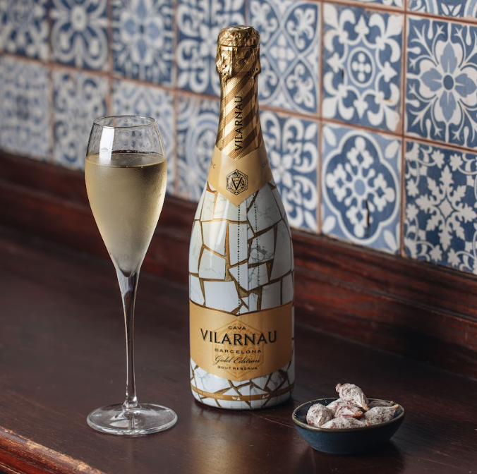 A glass of sparkling wine, a mosaic-patterned bottle labeled