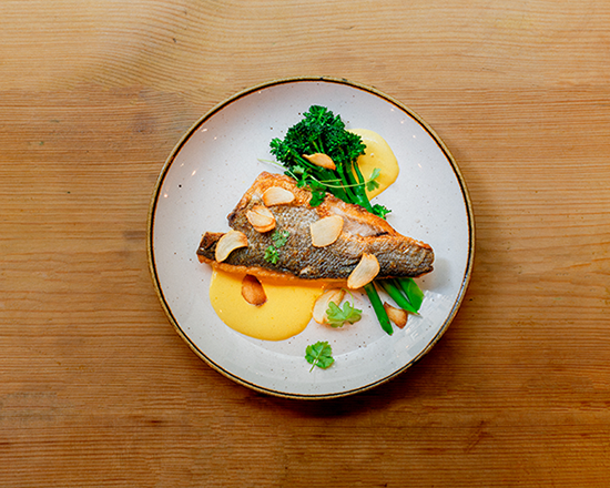 A rectangular fruit tart topped with sliced strawberries and cream sits on a plate next to a scoop of vanilla ice cream on a bed of cookie crumbs, all on a wooden table.